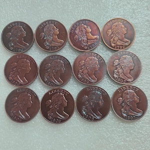 Peut inclure: Une collection de douze pièces de monnaie de couleur cuivrée. Chaque pièce représente un profil de femme aux cheveux flottants et le mot "LIBERTY". Les années 1796, 1797, 1798, 1799, 1800, 1801, 1802, 1803, 1804, 1805, 1806 et 1807 sont visibles.