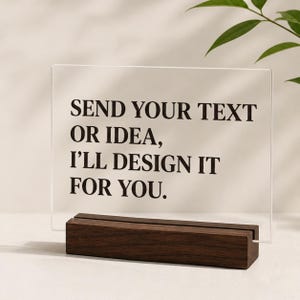 May include: A rectangular clear acrylic sign held in a dark brown wooden base. The sign features black text that reads: SEND YOUR TEXT OR IDEA, I'LL DESIGN IT FOR YOU. The display is positioned upright, showcasing a clean and simple design.