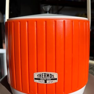 May include: A white ceramic mug with a black handle and the text "But First, Coffee" in a black, handwritten-style font. The mug is on a white surface.