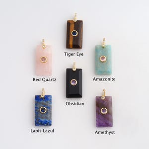 May include: A collection of rectangular gemstone pendants in various colors, including tiger eye, red quartz, amazonite, obsidian, lapis lazuli, and amethyst. Each pendant features a small, round gemstone and a gold-colored bail. The names of the gemstones are labeled.