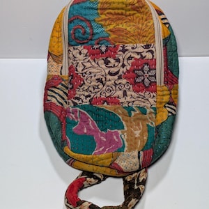 May include: A small, colorful backpack with a patchwork design. The bag features a variety of fabrics in shades of yellow, teal, red, and brown. It has a zipper closure and a handle. The bag measures approximately 8 inches in height.