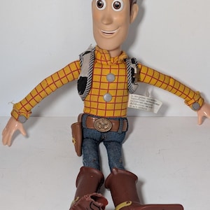 Puede incluir: Figura de acción de Woody de la franquicia Toy Story. La figura tiene una camisa a cuadros amarilla, vaqueros azules, un cinturón marrón con hebilla y botas de vaquero marrones. La figura lleva un chaleco y una funda con una pistola de juguete.