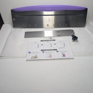 May include: A stainless steel cake leveler with a purple handle and inch measurements. Includes an additional blade and assembly instructions. The leveler is designed for precision cake decorating.