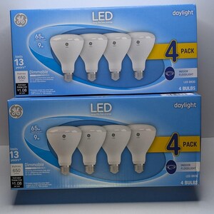 May include: Two blue cardboard boxes, each containing a 4-pack of GE LED BR30 indoor floodlight bulbs. The packaging displays the text LED, daylight, 65W replacement, 9W, lasts 13 years, 650 lumens, dimmable, and 4 bulbs. Each box shows four white bulbs.