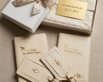 May include: A travel gift set featuring two cream-colored passport holders and two matching luggage tags with gold foil lettering. The items are presented in a white gift box with a snowflake ribbon and a card reading A curated adventure for ACJ & AWJ.