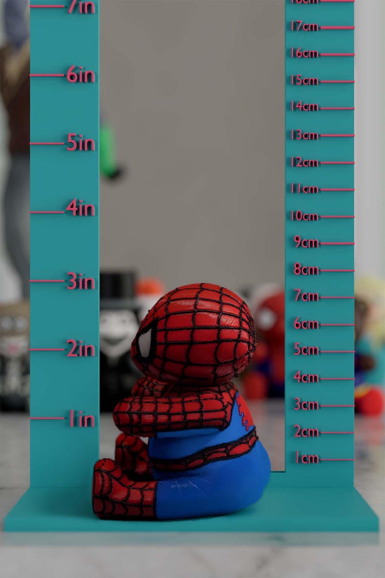 K&ouml;nnte beinhalten: Eine rot-blaue Spider-Man-Figur, etwa 7.6 cm hoch, sitzt vor einer t&uuml;rkisfarbenen Messlehre. Die Figur hat ein detailliertes Netzmuster auf dem Kopf und sitzt. Die Messlehre hat Zoll- und Zentimetermarkierungen.