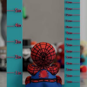 K&ouml;nnte beinhalten: Ein Spider-Man-Pl&uuml;schtier, etwa 15 cm gro&szlig;, sitzt vor einer t&uuml;rkisfarbenen Messwand. Das Spielzeug ist rot und blau, mit einem detaillierten Netzmuster auf dem Kopf. Die Tafel hat Zoll- und Zentimetermarkierungen.
