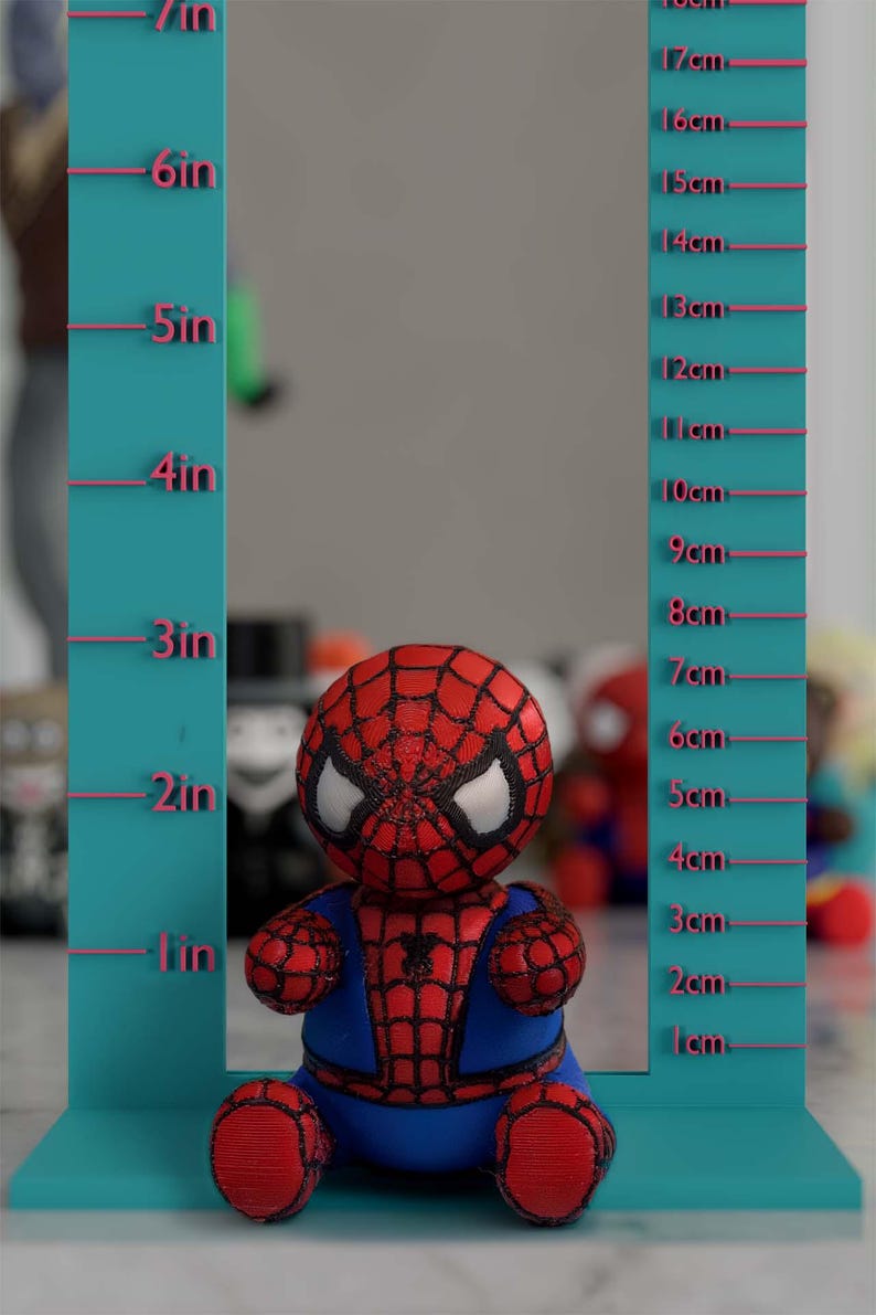 K&ouml;nnte beinhalten: Eine rot, blau und schwarz gehaltene Spider-Man-Figur, etwa 15 cm gro&szlig;, steht vor einem t&uuml;rkisfarbenen Messwerkzeug. Das Messwerkzeug hat Markierungen in Zoll und Zentimetern.