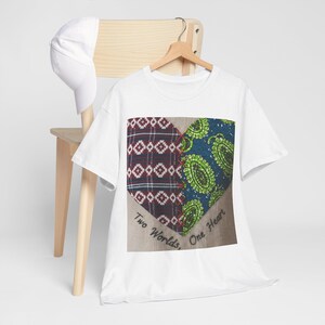 Könnte beinhalten: Weißes T-Shirt mit einem herzförmigen Design. Das Herz ist in zwei Teile geteilt: eines mit einem bordeauxroten und weißen geometrischen Muster und das andere mit einem blauen und grünen Paisley-Muster. Der Text "Two Worlds, One Heart" ist darunter aufgedruckt.