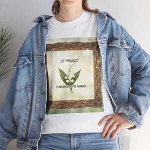 Könnte beinhalten: Weißes T-Shirt mit einem gerahmten Blumendesign, mit den Texten "LE MUGUET" und "NEVER SEEN ON THE INTERNET". Das Design zeigt eine Maiglöckchen-Illustration in einem dekorativen Rahmen. Die Person trägt eine Jeansjacke.