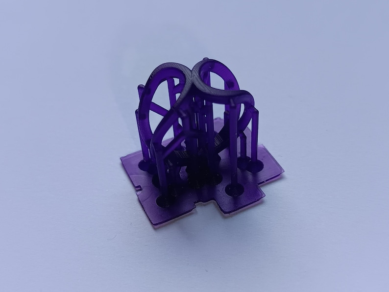 May include: A translucent purple 3D printed object featuring a flat square base with four circular cutouts and a central vertical structure composed of four curved, interconnected arch-like elements that meet at the top center point.