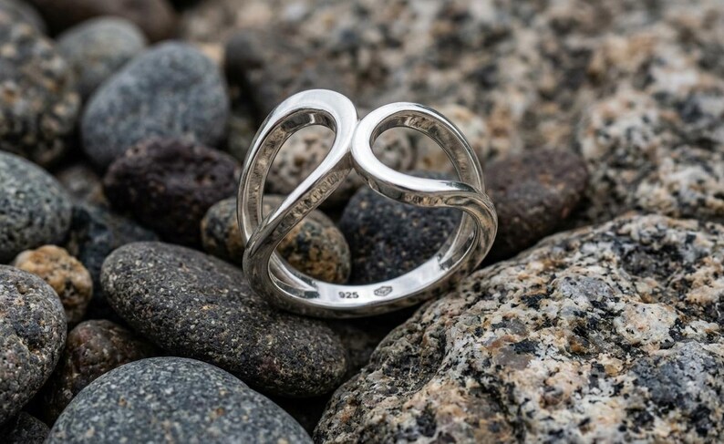 May include: A polished sterling silver ring featuring an open, intertwined loop design. The band is stamped with the 925 hallmark on the interior surface, indicating the silver content. The ring has a smooth, reflective finish throughout its structure.