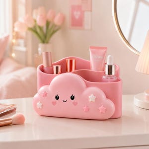 Puede incluir: Un organizador de maquillaje rosa en forma de nube con detalles de estrellas y corazones. El organizador contiene varios productos de belleza, incluyendo barras de labios, un frasco de sérum y un tubo de crema "Glowy". El organizador está sobre una superficie blanca.