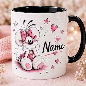 Könnte beinhalten: Ein weißer Keramikbecher mit schwarzem Innenraum und Henkel, verziert mit einer Cartoon-Maus mit rosa gepunkteter Schleife und Latzhose. Das Design zeigt rosa Herzen, Sterne und das Wort Name in schwarzer Schreibschrift mit rosa Unterstrich.