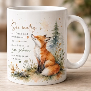 Könnte beinhalten: Ein weißer Keramikbecher mit einer Aquarellillustration eines Fuchses in einer Waldlandschaft. Der Text lautet: Sei mutig, sei frech und wunderbar. Das Leben ist zu schön, um angepasst zu sein. Das Design enthält kleine Herzen und Sterne.