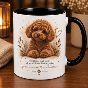 Könnte beinhalten: Ein weißer Keramikbecher mit schwarzem Innenraum und Henkel, bedruckt mit einem braunen Pudelwelpen, einem goldenen Herz, Blattmotiven und dem Text: Manchmal sind es die kleinen Pfoten, die die größten Spuren in unseren Herzen hinterlassen.