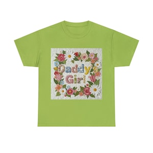 Könnte beinhalten: Hellgrünes T-Shirt mit floralem Design und der Aufschrift "Daddy's Girl". Das Design ist von einem Kranz aus Blumen umgeben, darunter Gänseblümchen, Rosen und Tulpen. Der Text ist in bunten Buchstaben gehalten.