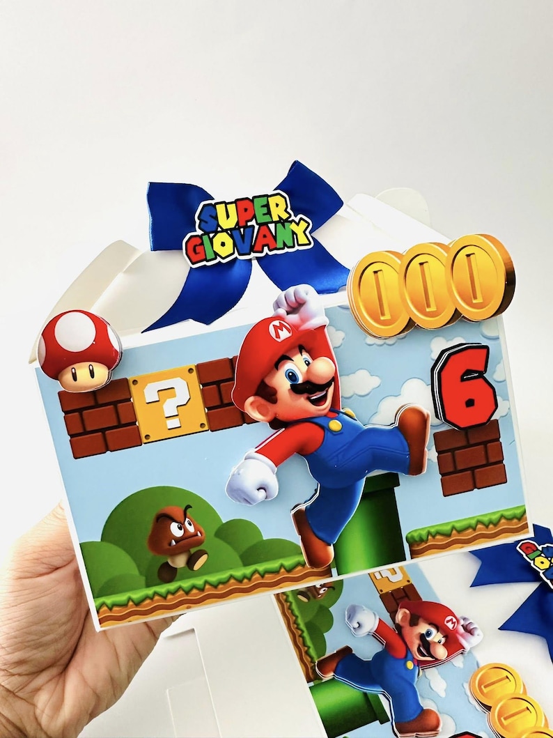 Op de afbeelding: Een versierde cadeauverpakking met een Super Mario-thema. De doos heeft een blauwe strik met de tekst "SUPER GIOVANY". De doos is versierd met Mario, munten, een paddenstoel en het cijfer 6. De achtergrond is een blauwe lucht met groene heuvels.