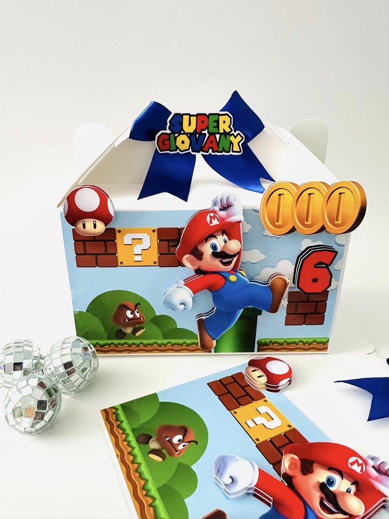 Op de afbeelding: Een witte geschenkdoos met een blauw lint en de tekst "SUPER GIOVANY". De doos heeft een cartoonillustratie van Mario die springt, samen met munten, paddenstoelen en het nummer 6. Extra decoratieve elementen zijn discoballen en een kaart met een gamethema.