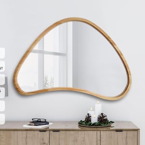 Puede incluir: Un espejo de madera orgánica oscura natural con una forma irregular. La profundidad del marco es de 30 mm y el grosor del espejo es de 4 mm. El espejo cuelga sobre un mueble de madera con cajones.