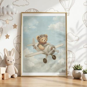May include: A framed print featuring a teddy bear wearing a pilot's helmet and scarf, flying a vintage airplane against a cloudy sky. The artwork has a soft, pastel color palette, evoking a whimsical, vintage aesthetic.