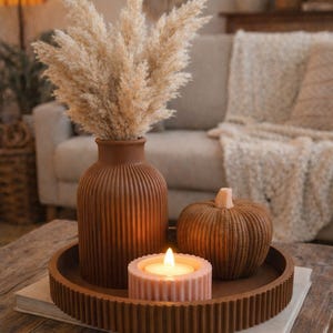 Peut inclure: Une composition décorative sur une table en bois. Elle comprend un vase marron avec des fleurs séchées, une citrouille, un bougeoir avec une bougie allumée et un plateau rond. Les articles sont dans des tons de marron et de beige.