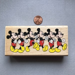May include: Wooden stamp featuring six Mickey Mouse characters walking in a line. The characters are black with red shorts and yellow shoes.