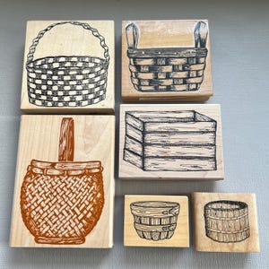 May include: Six wooden stamps with basket designs. The stamps show different basket styles, including woven and handled baskets, and a rectangular crate. The illustrations are in black and brown ink.