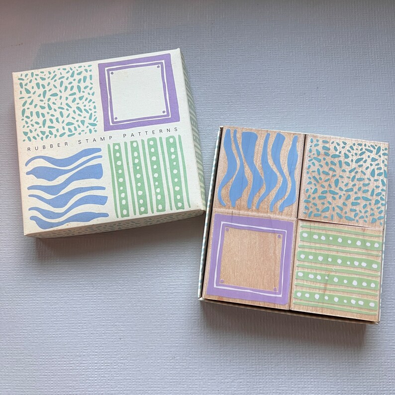May include: A set of four wooden rubber stamps with different patterns. The stamps are in a box with the words "Rubber Stamp Patterns" on the front. The patterns include waves, polka dots, stripes, and a speckled design.