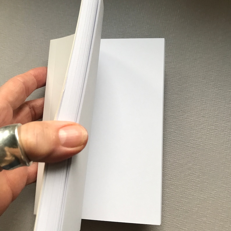 May include: A white blank notebook with a white cover and a white spine. The notebook is open to a blank page.