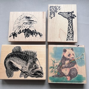 May include: Four wooden stamps with black and white illustrations of a bald eagle, a giraffe, a fish, and a panda bear eating bamboo. The panda stamp has the text "94 Arizona Stamps Tool" and "H-02 Panda Eating Bamboo".