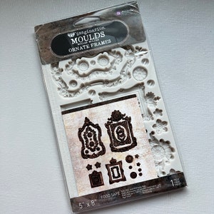 May include: A white silicone mold with intricate ornate frame designs. The mold is 5 inches by 8 inches and is food safe. The mold is labeled "Imaginarium. Moulds Ornate Frames".