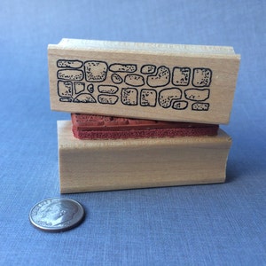 May include: Two wooden mounted rubber stamps, one with a design of a stone wall and the other with a red rubber surface.