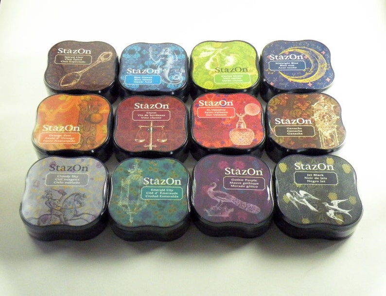 May include: Twelve ink pads in a variety of colors and designs. Each pad has a black plastic base and a square, slightly rounded, colorful top with a design and the word "StazOn" printed on it.