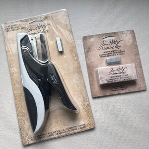 May include: A black and white mini tiny attacher stapler with a package of tiny attacher refills. The stapler and refills are in their original packaging. The packaging has the text "TINY ATTACHER" and "idea-ology".