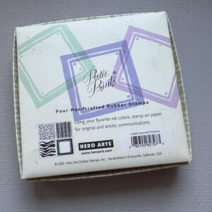 May include: A box of four handcrafted rubber stamps with the text "Poetic Prints" and "Hero Arts" on the front. The box is decorated with a green and purple design. The stamps are assorted patterns.