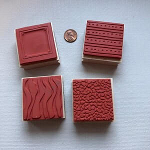May include: Four wooden mounted rubber stamps with different patterns. The patterns include a rectangle, wavy lines, small dots, and a pebble pattern. All the stamps are red.