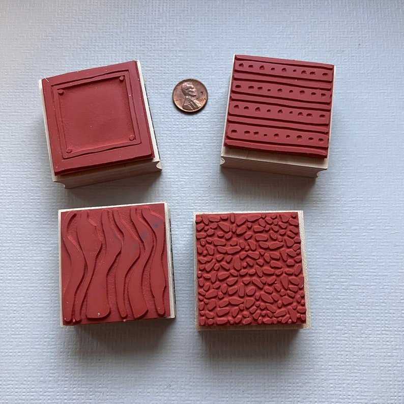 May include: Four wooden mounted rubber stamps with different patterns. The patterns include a rectangle, wavy lines, small dots, and a pebble pattern. All the stamps are red.