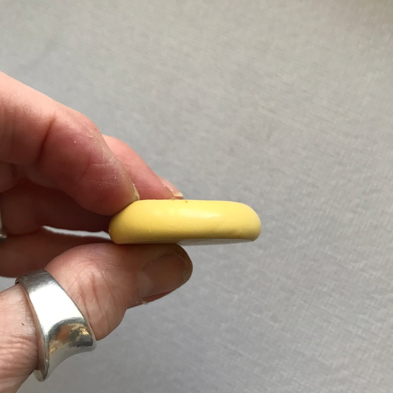 May include: A pale yellow ceramic button with a smooth, rounded surface.