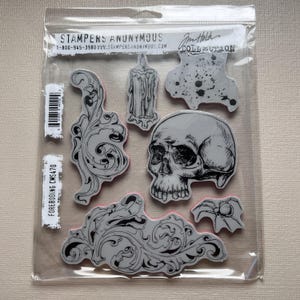 May include: Clear plastic package containing rubber stamps with gothic and Halloween themes. The stamps include a skull, a candle, ornate scrollwork, and a spider. The package has the text "STAMPERS ANONYMOUS" and "FOREBODING CMS470".