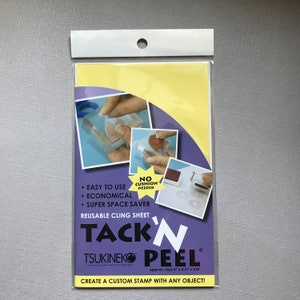 May include: A clear reusable cling sheet for creating custom stamps. The sheet is labeled "Tack 'n Peel" and "Tsukineko" with the text "Create a custom stamp with any object!"  The sheet is approximately 4 inches by 6 inches by 1/16 inches.