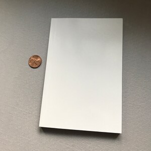 May include: A blank white card, approximately 10 cm by 15 cm, is lying flat on a textured grey surface. A copper penny is lying to the left of the card.