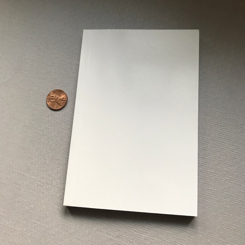 May include: A blank white card, approximately 10 cm by 15 cm, is lying flat on a textured grey surface. A copper penny is lying to the left of the card.