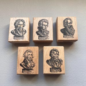May include: Five wooden stamps featuring portraits of famous composers: Beethoven, Mozart, Brahms, Haydn, and Schubert. Each stamp has the composer's name printed below the portrait.