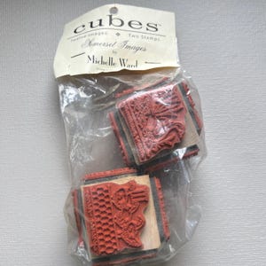 May include: A clear plastic bag containing red rubber stamps. The stamps are mounted on wooden blocks and have intricate designs. The bag's label reads "cubes" and "Somerset Images by Michelle Ward."