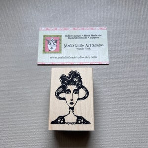 May include: Black and white rubber stamp featuring a woman with an octopus for hair. The stamp is mounted on a wooden block.