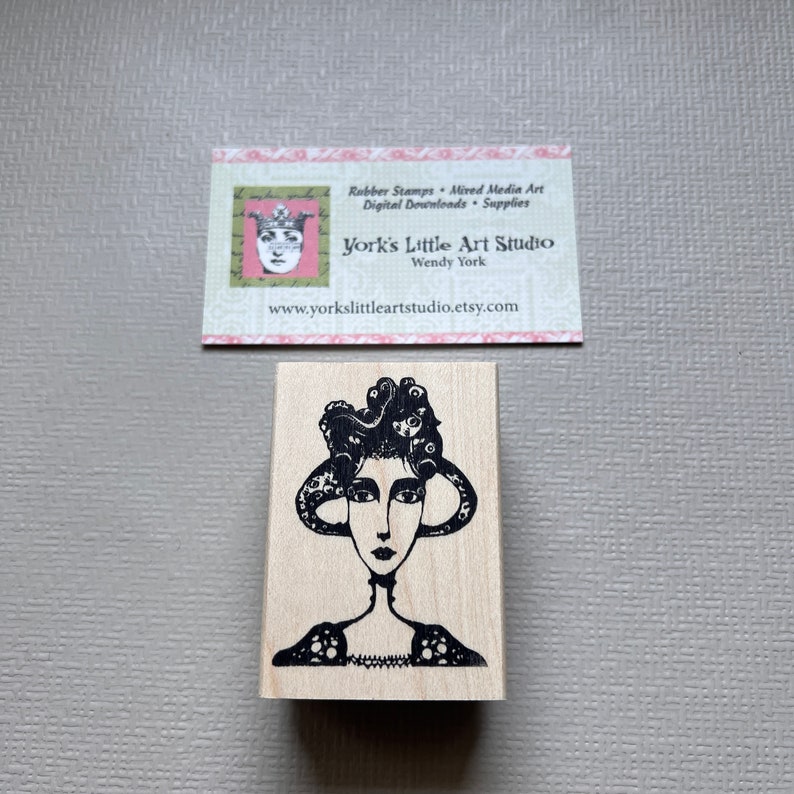 May include: Black and white rubber stamp featuring a woman with an octopus for hair. The stamp is mounted on a wooden block.