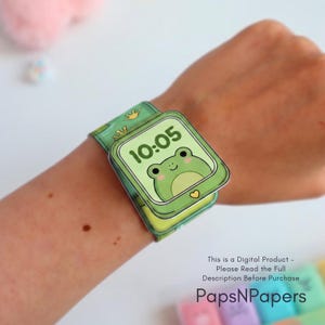 May include: A green paper watch with a frog illustration on the face displaying the time 10:05. The watch band features a repeating frog foot pattern. The text on the image reads: This is a Digital Product - Please Read the Full Description Before Purchase PapsNPapers.