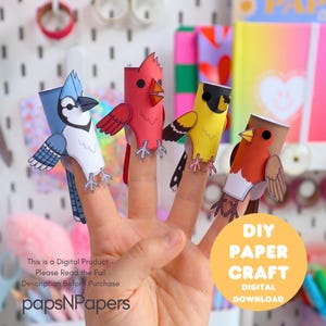 May include: Four paper finger puppets shaped like birds, including a blue jay, a red cardinal, a yellow goldfinch, and a brown robin. Each bird is crafted from paper and features distinct colors and markings. Text on image: DIY PAPER CRAFT.