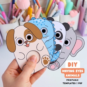 Peut inclure: Un ensemble de quatre découpages d'animaux en papier représentant un chien, un dinosaure bleu, un panda et un éléphant, chacun avec une découpe circulaire pour des yeux mobiles. Le texte DIY MOVING EYES ANIMALS PRINTABLE TEMPLATES | PDF est visible.